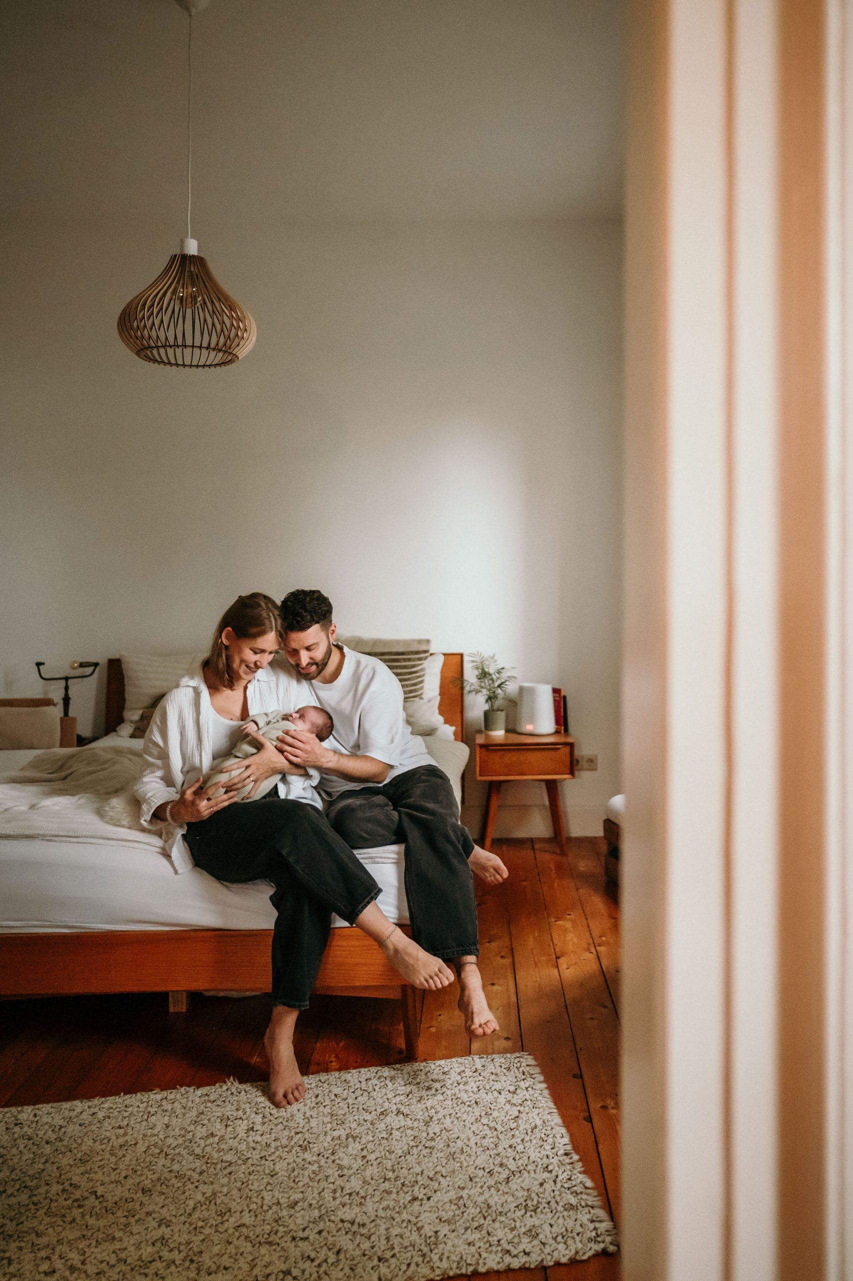 Eltern mit Baby bei Newborn Homestory, sitzend auf Bett