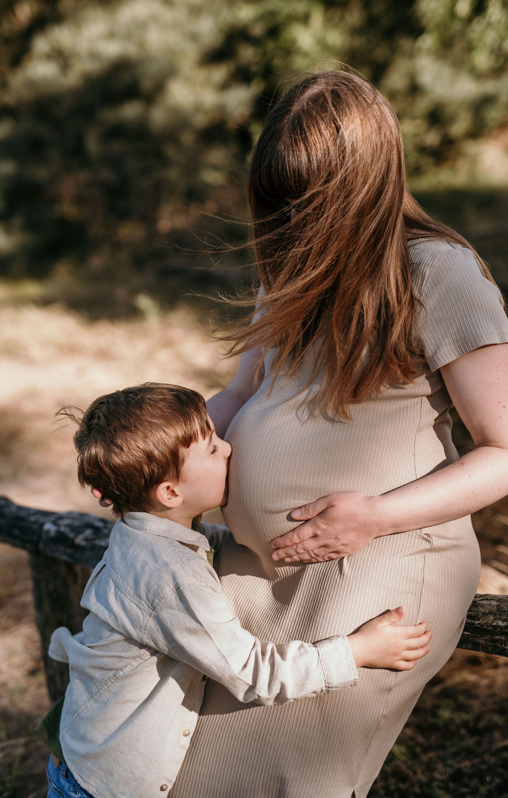 Schwangere Frau mit Kind, das ihren Bauch küsst, beim Babybauchshooting
