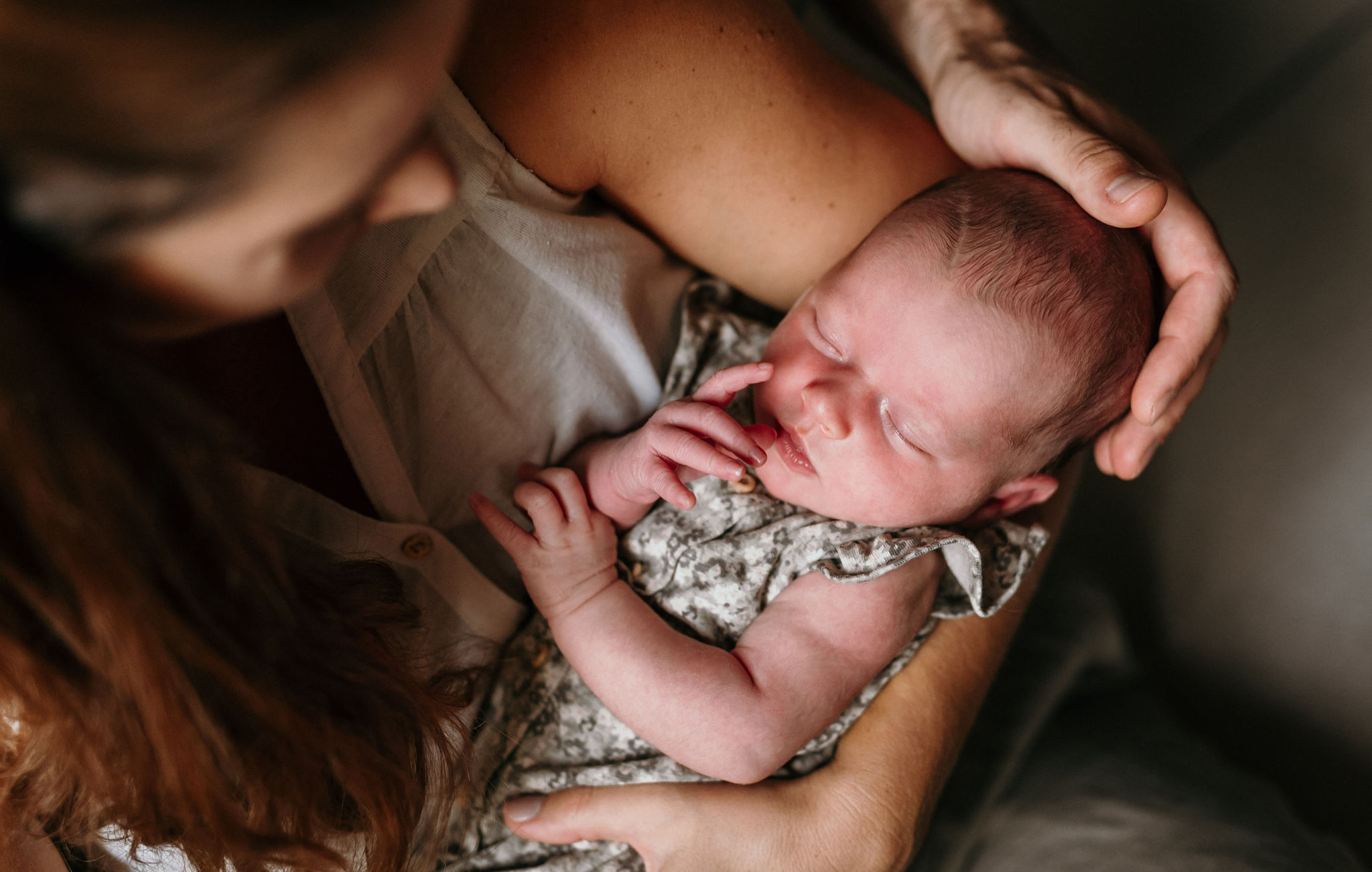 Mama hält ihr schlafendes Neugeborenes im Arm und legt die Hand an sein Köpfchen