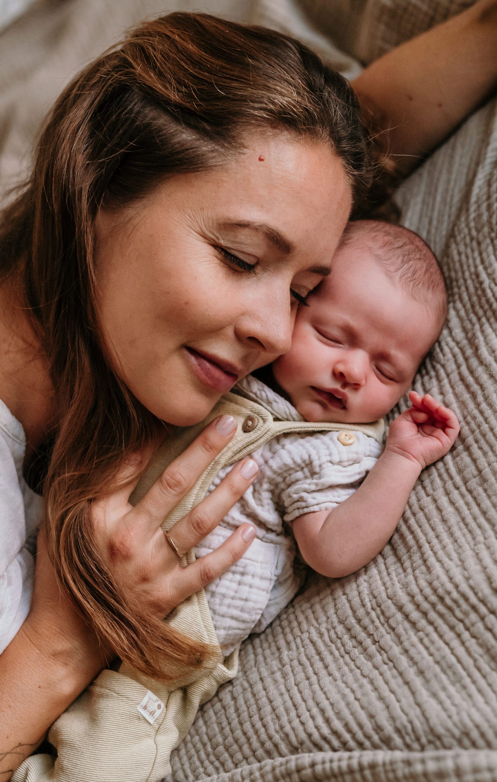 Mama schmiegt ihre Wange mit geschlossenen Augen an ihr schlafendes Neugeborenes