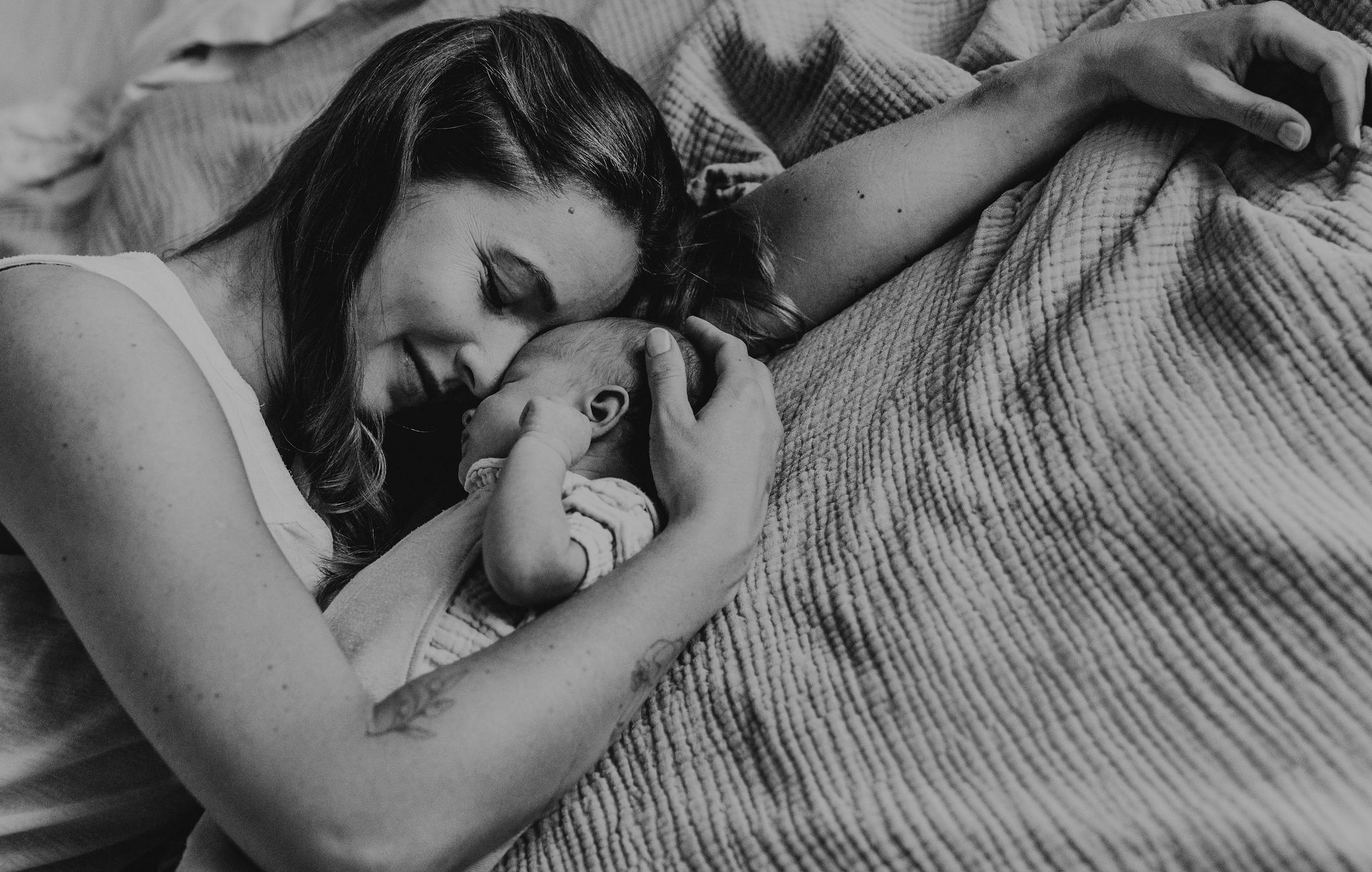 Mama liegt auf dem Bett und schmiegt ihr Gesicht an das Neugeborene, Schwarz-Weiß-Aufnahme