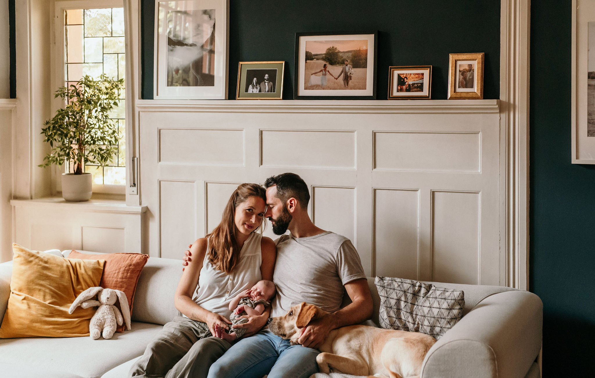 Familie mit Neugeborenem und Labrador auf dem Sofa vor der dunkelblauen Wohnzimmerwand in Bad Dürkheim
