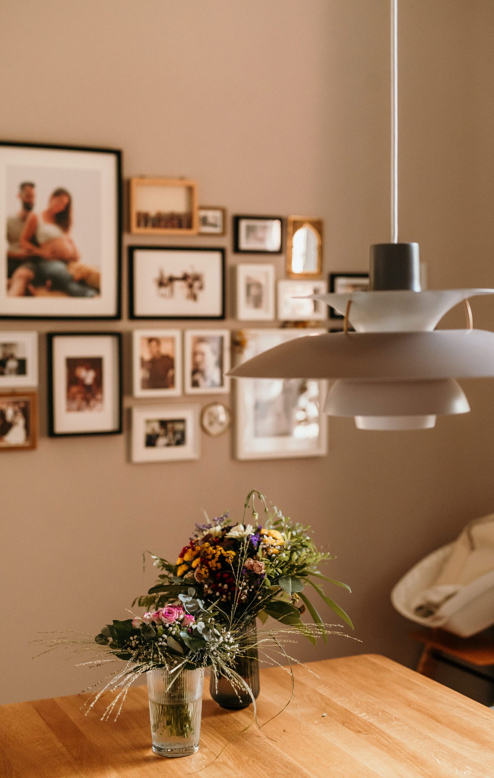 Esstisch mit Wiesenblumen im Glas vor einer Bilderwand mit Familienfotos im Zuhause in Bad Dürkheim