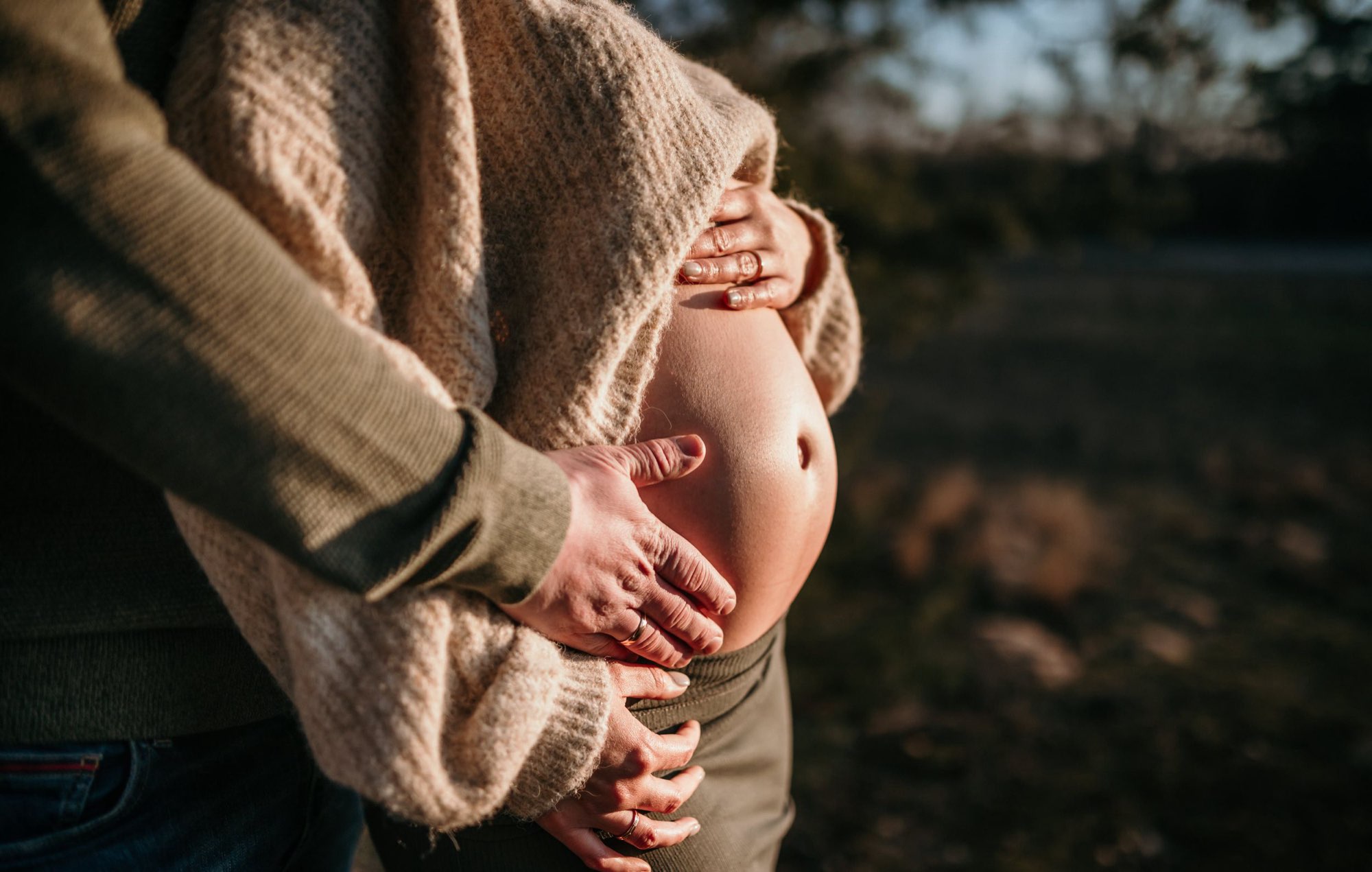 Paar hält gemeinsam liebevoll die Hände auf den nackten Babybauch