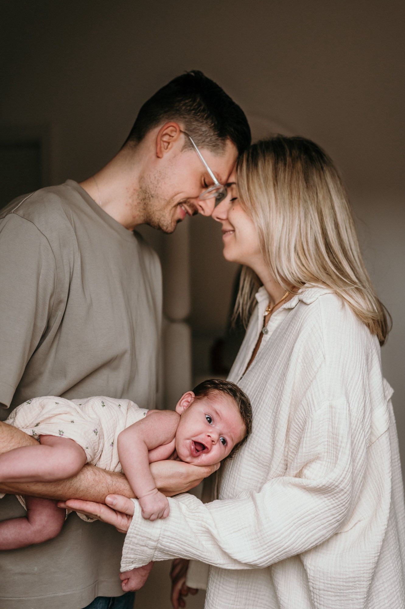 Eltern lächeln sich Stirn an Stirn an, Vater hält lachendes Baby
