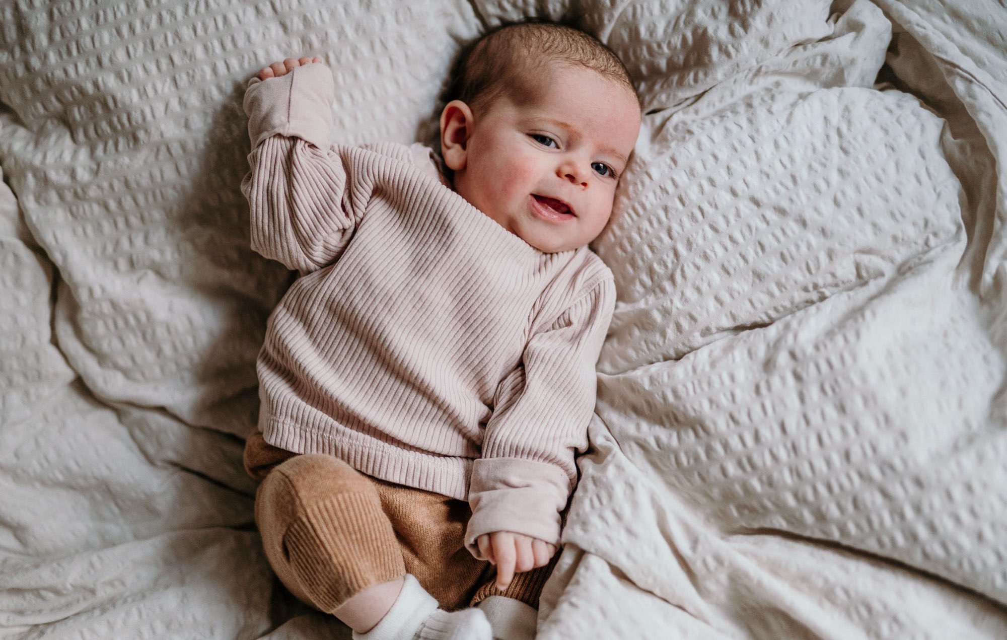 Baby im gestrickten Pullover lächelt fröhlich auf weichen Decken