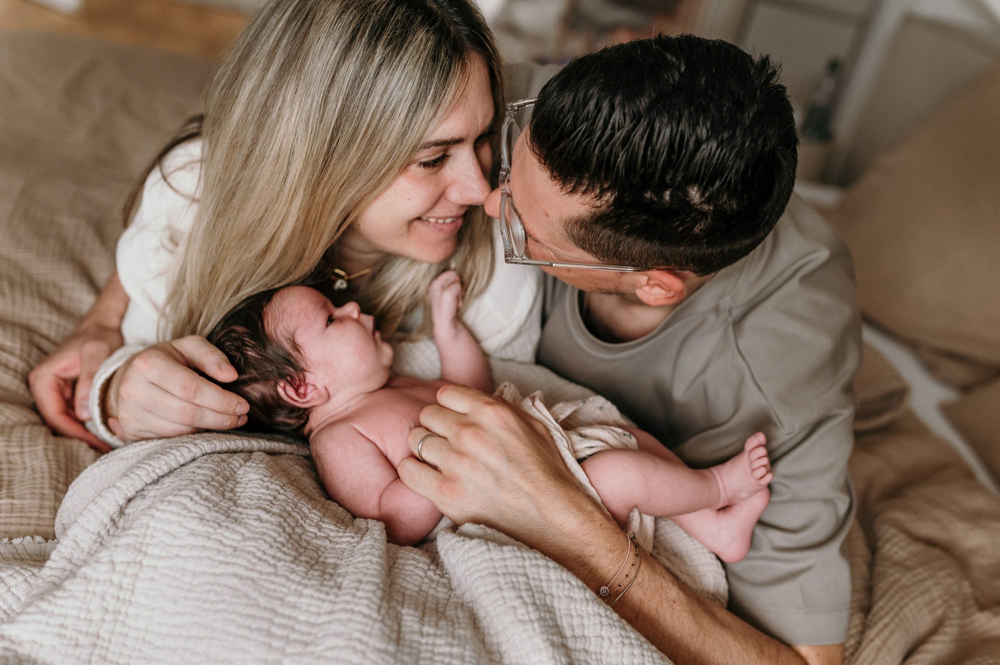 Eltern schmiegen sich liebevoll an ihr neugeborenes Baby im Bett