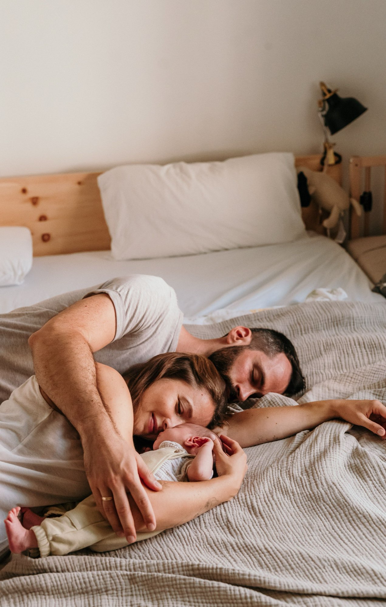 Eltern kuscheln entspannt im Bett mit ihrem Neugeborenen